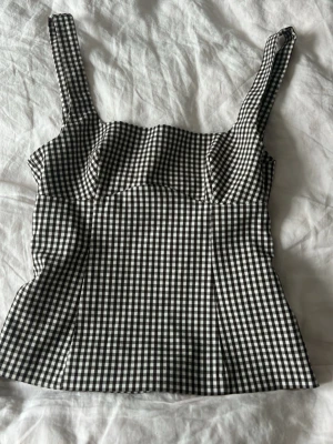 Rutig svartvit topp  - Supersnygg topp  från Zara med breda axelband i svart/brunt vitt  rutigt mönster. Toppen har en figurnära passform och knytning i ryggen för extra detalj. Perfekt att styla med jeans eller kjol för en trendig look. 