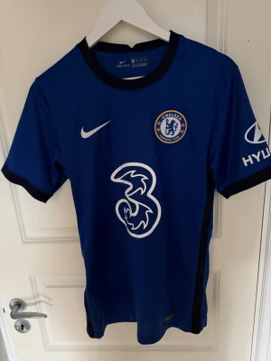 Chelsea FC matchtröja 2020/21 Nike   - Chelsea FC matchtröja i blått med vita detaljer och klubbmärke på bröstet. Tillverkad i lätt och ventilerande material med Nike-logga, sponsortryck och Hyundai-logga på ärmen. Perfekt för fotbollsträning eller att bära som supporter.