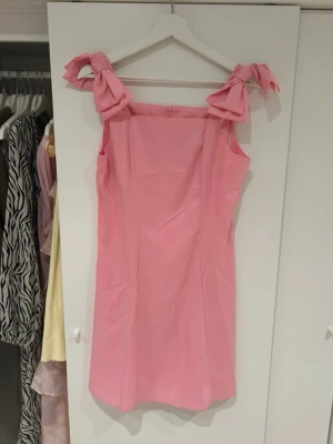 Rosa kort klänning - Söt rosa kort klänning med raka linjer och stora rosetter på axlarna. Aldrig använd 