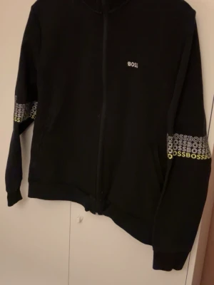 Svart zip hoodie från BOSS - Snygg svart hoodie från BOSS med dragkejda, dessutom finns det fina detaljer vid armbågarna. Tröjan är i bra skick inga noppor eller fläckar. Fastpris.
