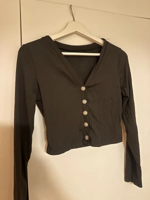 Svart kofta från SHEIN - Säljer en svart cardigan från SHEIN med långa ärmar och v-ringning. Koftan har fem knappar framtill och är gjord i ett stretchigt material med 5% elastan. Perfekt till lager på lager och enkel att styla. Koftan har några trådar vid axeln.