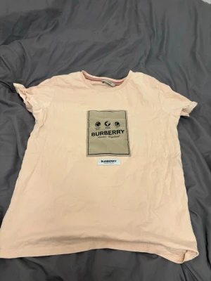 Beige Burberry t-shirt med tryck - Snygg beige t-shirt från Burberry med klassiskt tryck och logga på bröstet. T-shirten har rund halsringning och korta ärmar. Perfekt för dig som gillar stilrena plagg med exklusiv känsla.