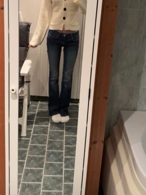 Blå bootcut jeans med kontrastsömmar - Säljer ett par blå bootcut jeans med snygga kontrastsömmar på bakfickorna. Jeansen har låg midja och klassisk femficksdesign. Dem har fått en litet hål under ena knät men det är lagat snyggt och det läggs inte märke till när man har dem på sig! Jag är 168 och dem passar perfekt i längden 