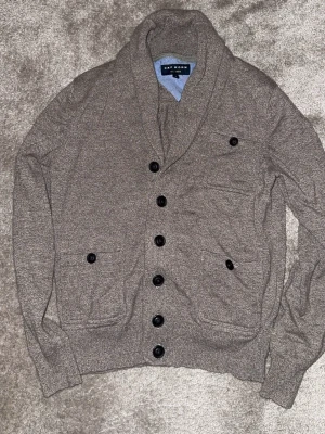 Grå kofta från Cape Horn - Snygg grå kofta från Cape Horn med sjalkrage och dubbelknäppning. Koftan har fyra framfickor med knappdetaljer och ribbade muddar vid ärmslut och nederkant. Perfekt för lager på lager och chill stil.