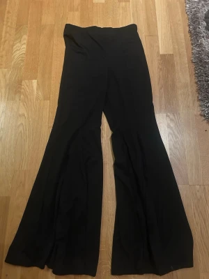 Svarta utsvängda leggings - Säljer ett par svarta leggings med hög midja och utsvängda ben. De har en enkel och stilren design utan synliga detaljer eller fickor. Perfekta för dig som gillar en trendig och bekväm look.