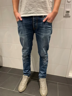 Vintage jeans tramarossa - Säljer ett par blå slim fit jeans från tramarossa med snygg tvätt och klassiska fem fickor. Jeansen har gul kontrastsöm och låg midja. Perfekta för dig som gillar en modern och avslappnad stil. Kontakta vid frågor! Missar en knapp som man inte tänker på och inte syns.