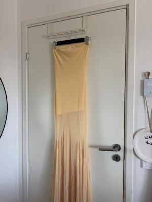 Ljusbeige långklänning i mjukt tyg - Säljer en elegant ljusbeige långklänning med släp och figurnära överdel. Klänningen har en mjukt fallande kjol och är ärmlös, perfekt för speciella tillfällen. Materialet känns lätt och följsamt mot kroppen.