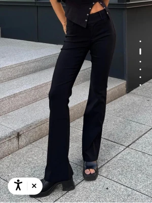 Svarta kostymbyxor med raka ben - Snygga svarta kostymbyxor med utsvängda ben. Byxorna har bälteshällor, knapp och dragkedja fram samt en ficka med lock bak. Perfekta för en clean och stilren look. Materialet ser ut att vara en mjuk och stretchig blandning.