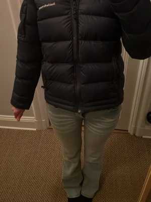 Svart pufferjacka från Peak Performance - Säljer en svart pufferjacka från Peak Performance med diskret logga på bröstet. Jackan har en klassisk boxig passform, dragkedja framtill och är vadderad för extra värme. 