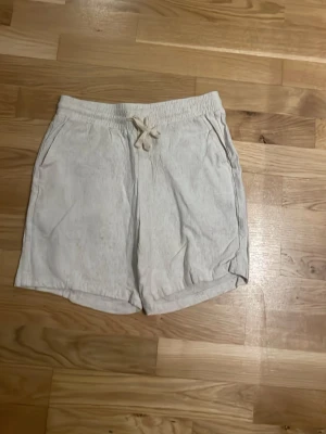 Beiga shorts från Grunt med snörning - Snygga beiga shorts från Grunt i mjukt material. De har elastisk midja med snörning och två sidofickor. Perfekta för varma dagar och chill stämning. Passar dig som gillar enkel och clean stil.