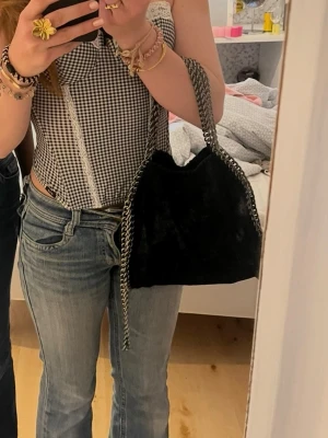 Svart axelväska med kedjedetaljer - Säljer en svart axelväska i mjukt material med silvriga kedjedetaljer längs kanterna och som axelrem. Väskan har en slouchy form och ger en cool vibe till vilken outfit som helst. Perfekt storlek för det viktigaste och enkel att matcha. Fick den från en kompis för två år sen men Fof i bra skick!