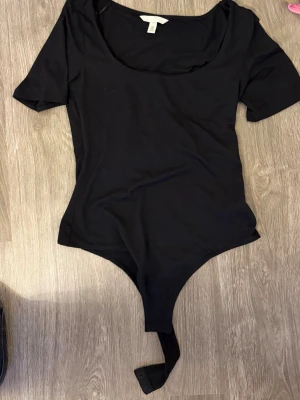 Svart body från H&M med kort ärm - Enkel och stilren svart body från H&M med korta ärmar och rund halsringning. Tillverkad i mjukt och stretchigt material för en bekväm passform. Perfekt att matcha med jeans eller kjol för en snygg look.