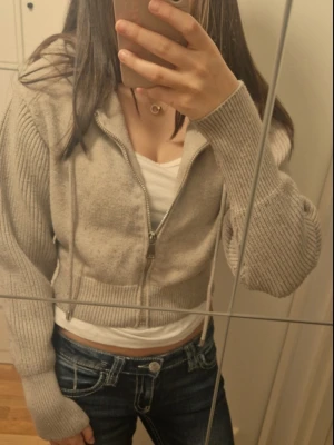 Beige stickad hoodie från ZARA - Säljer en beige stickad hoodie från ZARA med dragkedja framtill och ribbade muddar. Hoodien har dragsko i huvan och är croppad i modellen. Perfekt för en chill och avslappnad stil.