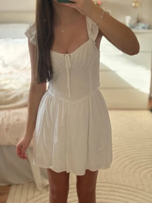 Vit gullig klänning med knytning bak  - Söt vit klänning med knytningbak, finns undershorts och även fickor på sidan av klänningen så du slipper ha väska!! Endast använd en gång, så super skick. Passar perfekt till konfirmation, skolavslutning eller midsommar🩷💐