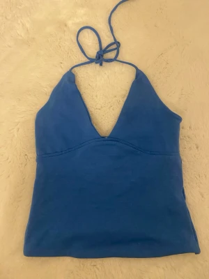 Blå halterneck linnetopp - Snygg blå halterneck linnetopp med knyt i nacken och djup v-ringning. Toppen är ärmlös och har en enkel, stilren design som passar perfekt till sommaren. Tillverkad i mjukt bomullsmaterial för en bekväm känsla.