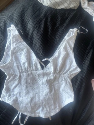 Vit broderad linnetopp med snörning - Söt vit linnetopp med broderade blommor och v-ringning. Och en knut i ryggen. Köpt ifrån Zara och använt 1-2 gånger. Passar nog för S-M fast mot det mesta M