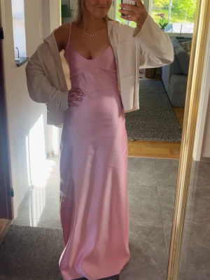 Ljusrosa satinklänning - Säljer en lång, ljusrosa satinklänning med smala axelband och v-ringning. Den är från märket by Stina köpt förra året. Den är i storlek M, men för för stor i midjan så den är insydd. Så lite mindre än vanlig M. Jag är 180 ungefär så passar bra om man är längre. Är nog enkelt att sy upp den också. Andvänd 1 gång 