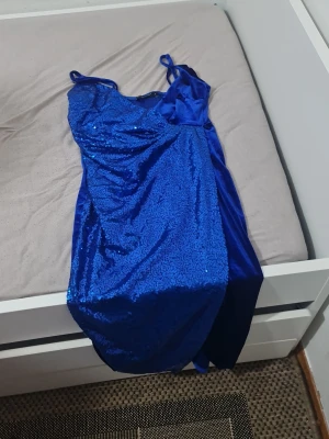 Blå paljettklänning Double Crazy - Snygg blå klänning från Double Crazy i storlek S. Klänningen har smala axelband och är dekorerad med glittriga paljetter på framsidan. Materialet är glansigt och ger en lyxig känsla, perfekt för dig som vill sticka ut.
