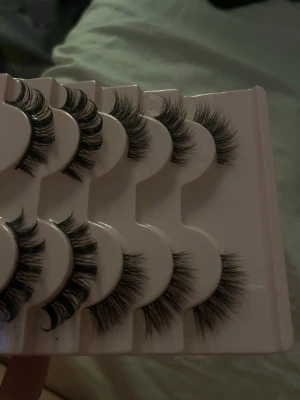 Fylliga svarta lösögonfransar 5-pack - Säljer ett 5-pack med fylliga och dramatiska svarta lösögonfransar. Fransarna har en böjd form och sitter på en vit plastbricka. Perfekta för dig som vill ha extra volym och längd till fransarna. Materialet är syntetiskt och ger en naturlig look.