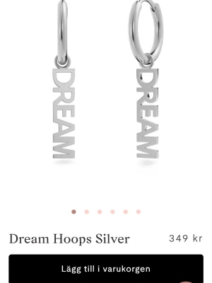 Dream hoops i silver Edblad - Snygga örhängen i silverfärg med texten 'DREAM' som hängande detalj. Runda hoops med modern och stilren design, perfekta för att ge din look en cool touch. Tillverkade i metall med blank finish. Från Edblad orginal pris 349 säljer för 249 då dom är använda fåtal gånger ❤️
