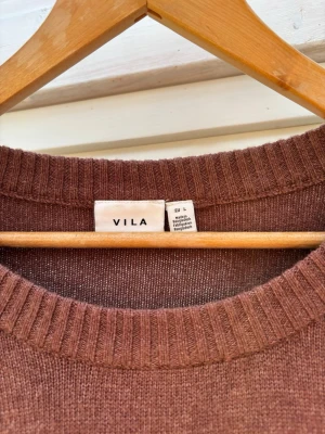 Brun stickad tröja från Vila - Mysig brun stickad tröja från Vila med rund halsringning och ribbade muddar vid ärmslut och nederkant. Perfekt för lager på lager och enkel att matcha med jeans eller kjol. Mycket fint skick men i nedre vänstra kant på baksidan är den smått nopprig men det syns knappast när den sitter på. Storlek L men passar även mindre!