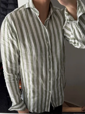 Randig linneskjorta från John Henric - Snygg skjorta från John Henric i ljusgrönt och vitt med vertikala ränder. Tillverkad i luftig linne, perfekt för varmare dagar. Klassisk krage, knäppning framtill och långa ärmar. Skjortan har en relaxed och stilren look.