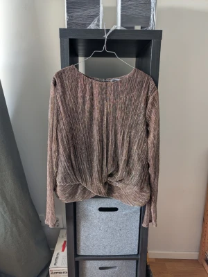 Glittrig brun långärmad topp Gallery - Säljer en glittrig brun långärmad topp från Gallery med twistad detalj framtill. Toppen har en lös passform och är tillverkad i ett skimrande syntetmaterial som fångar ljuset snyggt. Perfekt för dig som vill sticka ut lite extra.