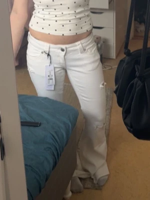 Vita bootcut jeans från Gina  - Säljer ett par vita bootcut jeans från Gina med slitningar vid knäet och klassiska fem fickor. Jeansen har låg midja och är tillverkade i ett stretchigt denimtyg för en bekväm passform. Perfekta för en trendig och avslappnad look.