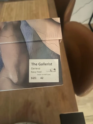 The Gallerist Geneva Navy Heel sneakers - Snygga vita sneakers från The Gallerist, modell Geneva Navy Heel. Skorna har en mörkblå häl och en svart klöverdetalj på sidan. Tillverkade i Portugal i läder med vita snören och klassisk låg profil.