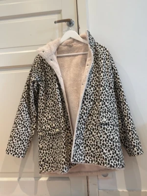 Leopardmönstrad regn/pälsjacka - Säljer en snygg leopardmönstrad pälsjacka/regnjacka med mjukt, ljust foder. Jackan har två fickor framtill och stängs med tryckknappar. Perfekt för dig som vill sticka ut och hålla dig varm under vintern. Materialet är fuskpäls och jackan har en rak passform.