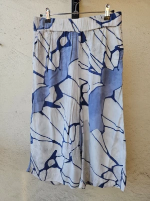 Vita linnebyxor med blått mönster - Luftiga och vida sommarbyxor från Wera i fint mönster i blått och vitt. Kortare modell. Storlek 34.