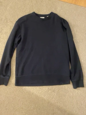 Mörkblå basic sweatshirt - En stilren mörkblå sweatshirt med rund hals och långa ärmar. Tröjan har en enkel design utan tryck eller mönster och är tillverkad i mjukt material, perfekt för en avslappnad look.