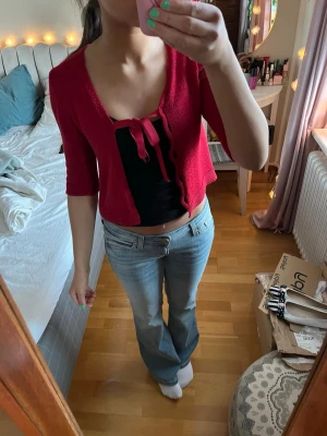 Röd stickad bolero med knytband - Kort röd stickad bolero med trekvartsärm och söt knytning framtill. Den e köpt second hand vet inte original märket. Men väldigt bra skick!  