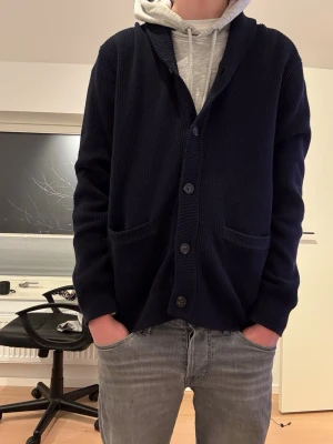 Mörkblå kofta från Bondelid - Snygg mörkblå kofta från Bondelid med knäppning framtill och två fickor. Koftan har ribbstickad struktur och en avslappnad passform, perfekt att slänga över en hoodie eller t-shirt. Klassisk och enkel design som funkar till det mesta. Köptes för 800 kr och använd 1 gång