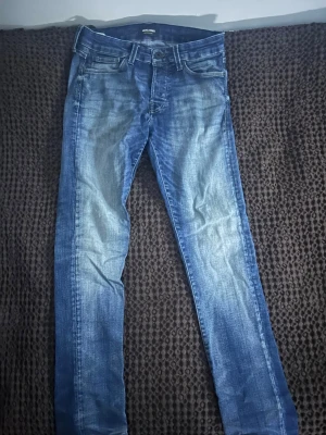 Blå slim jeans från Jack & Jones - Snygga blå slim fit jeans från Jack & Jones med klassisk femficksdesign och slitna detaljer framtill. Jeansen har normal midja och raka ben, perfekta till en avslappnad stil. Tillverkade i mjuk bomull för skön känsla. Storlek W30 L32