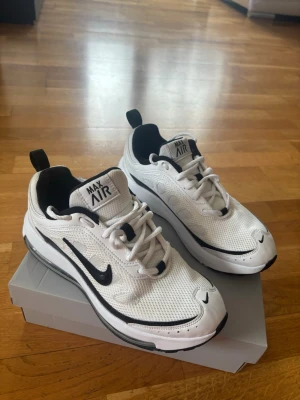 Nike Air Max vita sneakers - Nike Air Max sneakers i vitt meshmaterial med svarta detaljer och svart swoosh på sidorna. Skorna har en sportig siluett, synlig Air Max-dämpning i sulan och dragflikar bak. Perfekta för en streetwear-look.