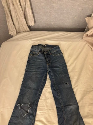 Blå slitna bootcut jeans från Gina  - Säljer ett par blå bootcut jeans med slitningar och hål på benen, som jag har gjort själv. Säljer dom för att jag har tröttnat på dom priset är som det är eftersom jag har gjort hålen själv och missfärgning lägnst ner på dom som du ser på sista bilden, har även använt ganska mycket innan. Nypris 500kr.