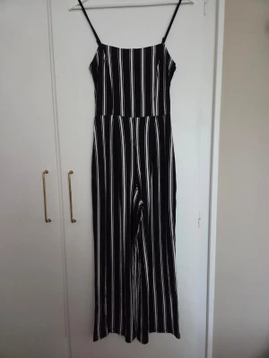 Svartvit randig jumpsuit med smala band - Svart jumpsuit med vita ränder och smala axelband. Vida ben och rak passform. 