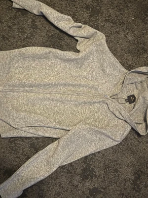 Grå stickad zip-hoodie från NEXT XS - Snygg gråmelerad hoodie från NEXT i storlek XS. Tröjan har dragkedja framtill, huva och två sidofickor. Perfekt för en chill och avslappnad stil. Materialet är mjukt och skönt, passar perfekt till vardags eller när du vill vara bekväm.
