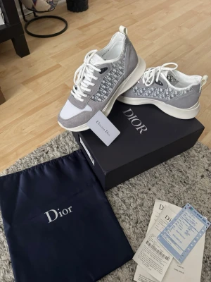 Gråa Dior sneakers med monogram - Snygga sneakers från Dior i grått och vitt med klassiskt Dior-monogram på sidorna. Skorna har vita snören, tjock vit sula och detaljer i mocka och mesh. Perfekta för dig som vill ha en lyxig och trendig look. Storlek 44 men passar 43 också och priset kan diskuteras 