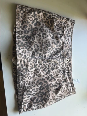 Leopardmönstrad kjolbomull - Snygg kjol  med leopardmönster i beige och svart. Klassisk femficksmodell med knapp och dragkedja framtill. Perfekta för dig som vill sticka ut lite extra i sommar.