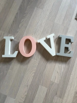 Dekorativa bokstäver LOVE i trä - Säljer fyra fristående bokstäver i trä som tillsammans bildar ordet LOVE. Bokstäverna är målade i vitt och ljusrosa, perfekta som dekoration i hemmet eller till fest. Stilren och modern design som passar på hyllan eller bordet. 