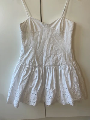 Vit somrig klänning med broderade detaljer - Säljer denna populära söta, vita kortklänning med smala axelband och broderade håldetaljer längst ner på kjolen från zara. Helt slutsåld. Aldrig använd så väldigt bra skick. Klänningen har inbyggda shorts. 💕