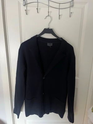 Mörkblå stickad kofta från H&M - Stilren mörkblå stickad kofta från H&M med två framfickor och enkelknäppning. Klassisk passform med mjukare material som ger en avslappnad look. Perfekt till jeans eller chinos för en snygg outfit.