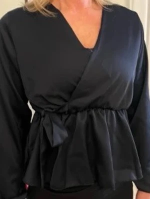 Missay marinblå omlottblus med volang - Stilren marinblå omlottblus med långa ärmar och markerad midja med knytband. Blusen har volang nertill och djup v-ringning. Perfekt för dig som gillar en feminin och trendig look.