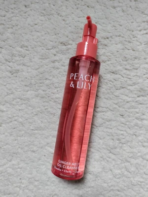 Peach & Lily toner i rosa flaska - Fräsch toner från Peach & Lily i en genomskinlig rosa plastflaska med pump. Flaskan är cylindrisk och har en modern design med vit text. Perfekt för att fräscha upp huden i din hudvårdsrutin.