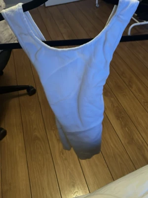 Vit ribbad body med djup rygg - Säljer en vit body i ribbat material med breda axelband och djup rygg. Bodyn har en tight passform och är tillverkad i stretchigt tyg som sitter snyggt på kroppen. Perfekt att styla med jeans eller kjol för en trendig look.