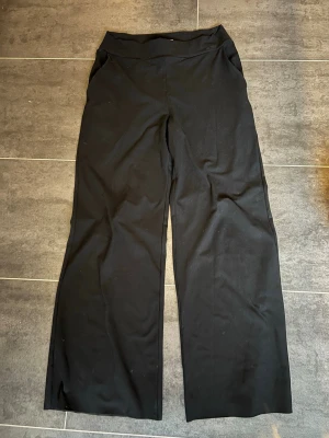 Svarta vida byxor med hög midja från Aimn  - Svarta byxor med hög midja och vida ben. Byxorna har en enkel design med rymliga fickor men utan särskilt synliga. De är tillverkade i ett mjukt, stretchigt tyg som ger en bekväm känsla. Perfekta för en avslappnad och stilren look.