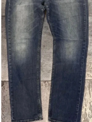 Mörkblå raka jeans med slitningar - Mörkblå jeans med raka ben och diskreta slitningar framtill. Jeansen har klassisk femficksdesign och ljusare tvättade partier på låren. Materialet är denim i bomull. Perfekta för en avslappnad och trendig look.