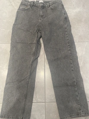 Grå relaxed jeans från Grunt  - Säljer ett par gråa jeans från Gina Tricot med rak passform och klassisk femficksdesign. Jeansen har hög midja och är tillverkade i ett slitstarkt denimtyg. Perfekta för en avslappnad och trendig look.